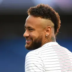 Sonrisa de Neymar con su característico peinado mohicano, luciendo una camiseta a rayas blancas y rojas.
