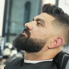 Hombre con barba y un moderno corte de pelo con degradado, uno de los tipos de corte de pelo hombre más populares.