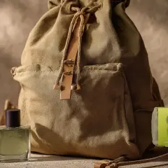 Botella de colonia Viento de Mercadona junto a una mochila de lona, lista para una aventura.
