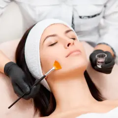 Una esteticista aplica un tratamiento de peeling facial con brocha a una mujer.