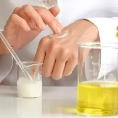 Manos de científico aplicando crema, con probetas y plantas. El cetearyl alcohol es clave en esta formulación.