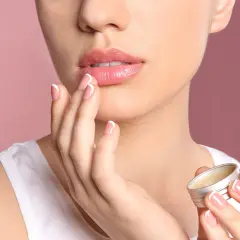 Mujer aplica bálsamo para aliviar labios secos. Sus manos y uñas perfectas contrastan con la suavidad de sus labios.