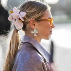 Mujer con coleta adornada con una flor de tela y pendientes de pétalos, luciendo gafas naranjas y una chaqueta de cuero.