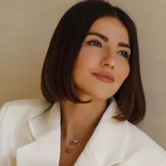 Mujer con un corte de pelo **italian bob**, blazer blanco y collares delicados.