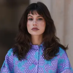 Mujer con melenas cortas con volumen, flequillo y un llamativo abrigo morado y turquesa.