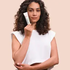 Mujer con cabello rizado sostiene un tubo de Cicalfate, crema reparadora para la piel.