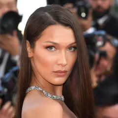 Bella Hadid con un elegante side part, luciendo un collar de diamantes y rodeada de fotógrafos.