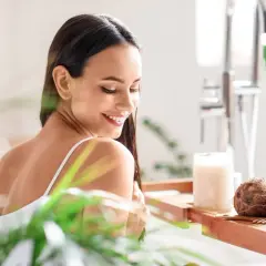 Mujer sonriente en la bañera con cocos y un frasco de aceite de coco, mostrando para qué sirve el aceite de coco para el cabello.