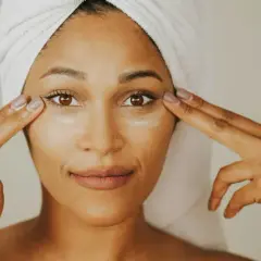 Mujer con toalla en la cabeza aplica crema con ceramida alrededor de sus ojos.