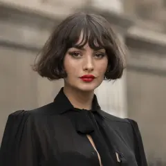 Mujer con un elegante corte de pelo **french bob**, labios rojos vibrantes y un top negro con lazada.