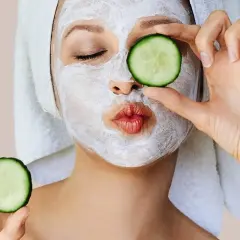 Mujer con mascarillas caseras para la cara y rodajas de pepino, lista para un spa en casa.
