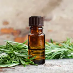 Aceite esencial de romero para el pelo, con ramitas frescas de romero sobre madera rústica.