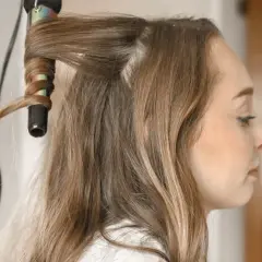 Creando peinados fáciles y rápidos: una mano riza el cabello de una mujer con una plancha.
