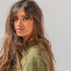 Mujer con cabello castaño largo y ondulado, con flequillo cortina que enmarca su rostro.