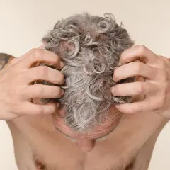 Hombre rascándose el cuero cabelludo con pelo gris y rizado.