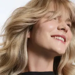 Mujer sonriendo con cabello rubio claro ondulado y brillante.