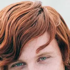 Ojos verdes y cabello pelirrojo ondulado, con pecas visibles en la piel.