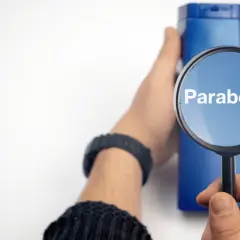 Lupa amplía la palabra "Parabens" sobre un frasco azul, indicando la búsqueda de ingredientes en productos.