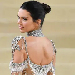 Mujer con un elegante moño recogido, luciendo un vestido de pedrería y un collar brillante.