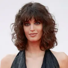 Mujer con curly pelo corto rizado natural, mirada intensa y vestido negro brillante.