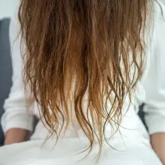 Cabello castaño, con puntas secas y aspecto de pelo quemado, cayendo sobre una bata blanca.