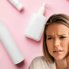 Mujer con expresión de duda rodeada de envases de cosméticos, algunos con diseño ondulado.