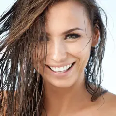 Mujer sonríe con pelo efecto mojado, luciendo natural y radiante.