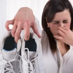 Mujer tapándose la nariz por el fuerte olor de pies que emana de unas zapatillas blancas.