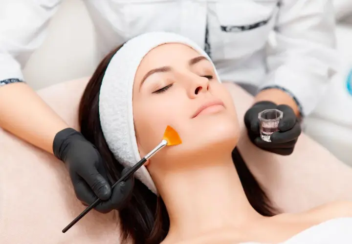 Una esteticista aplica un tratamiento de peeling facial con brocha a una mujer.