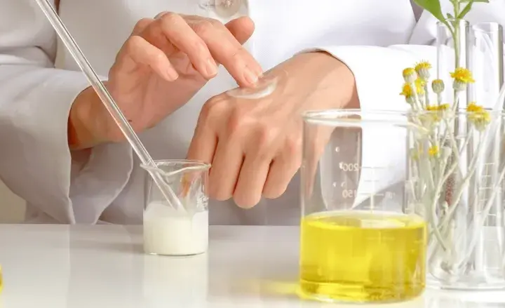 Manos de científico aplicando crema, con probetas y plantas. El cetearyl alcohol es clave en esta formulación.