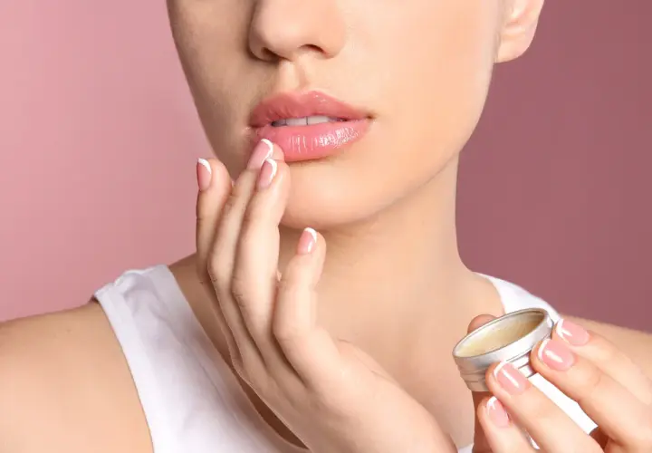 Mujer aplica bálsamo para aliviar labios secos. Sus manos y uñas perfectas contrastan con la suavidad de sus labios.