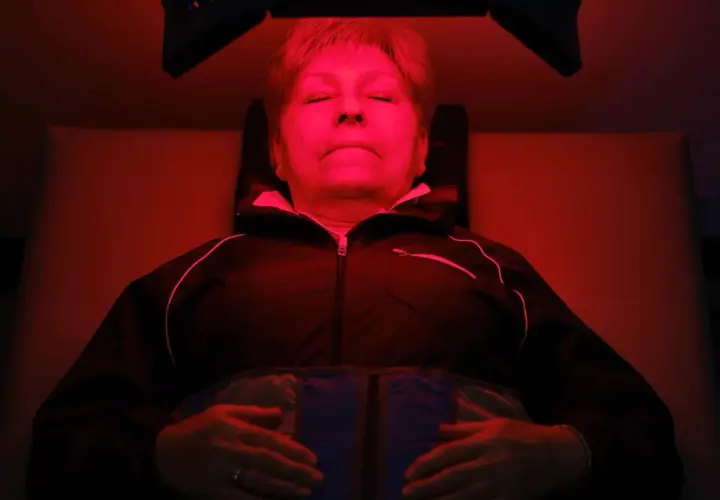 Mujer relajada bajo luz roja, experimentando los beneficios de la terapia de luz para el bienestar.