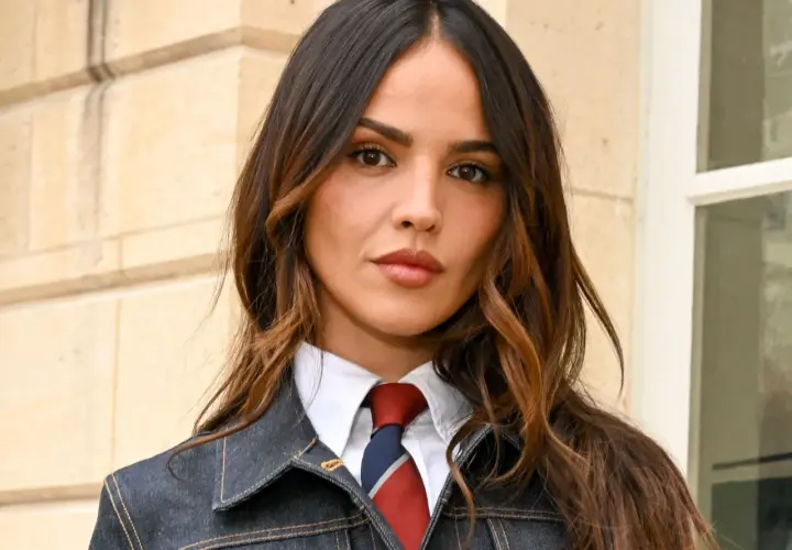 Mujer con cabello castaño y mechas woodlights, viste camisa blanca, corbata y chaqueta vaquera.
