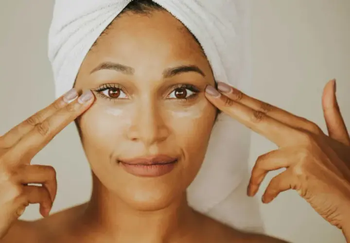 Mujer con toalla en la cabeza aplica crema con ceramida alrededor de sus ojos.