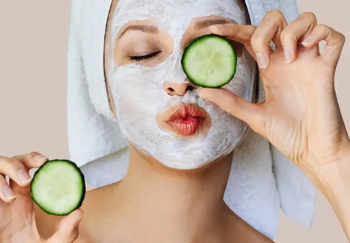 Mujer con mascarillas caseras para la cara y rodajas de pepino, lista para un spa en casa.