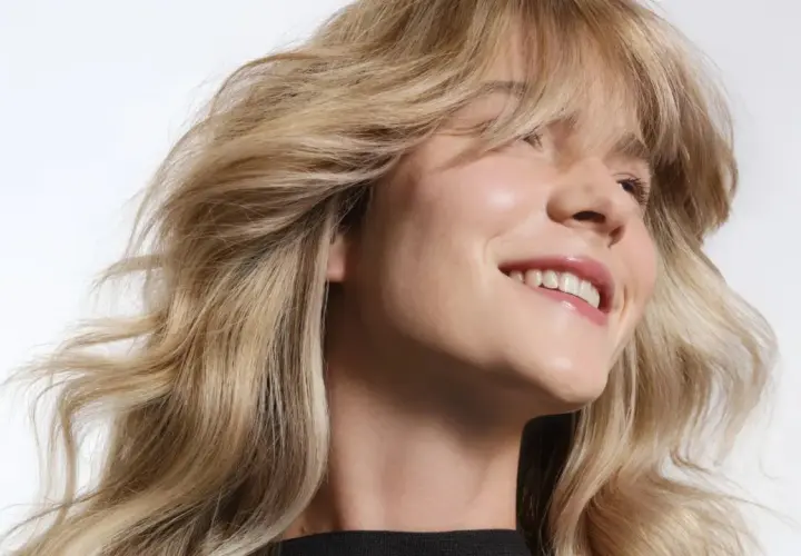 Mujer sonriendo con cabello rubio claro ondulado y brillante.