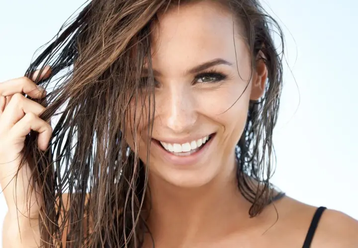 Mujer sonríe con pelo efecto mojado, luciendo natural y radiante.