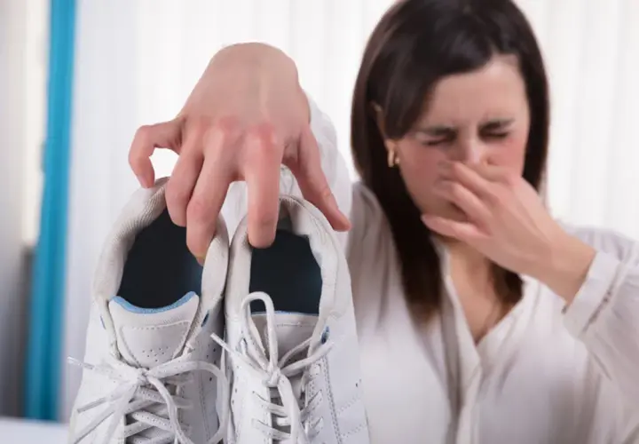 Mujer tapándose la nariz por el fuerte olor de pies que emana de unas zapatillas blancas.