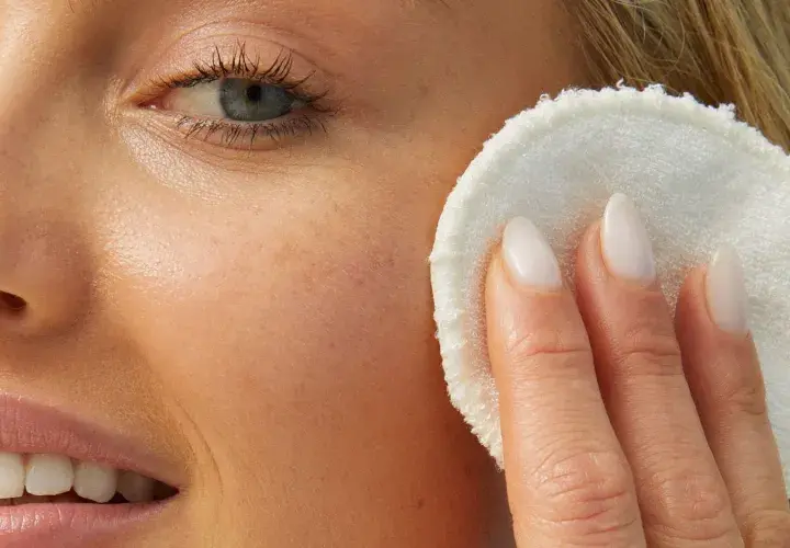 Rostro de mujer rubia con piel luminosa, aplicándose un disco desmaquillante. Su piel luce sin imperfecciones, sin rastro de milium.