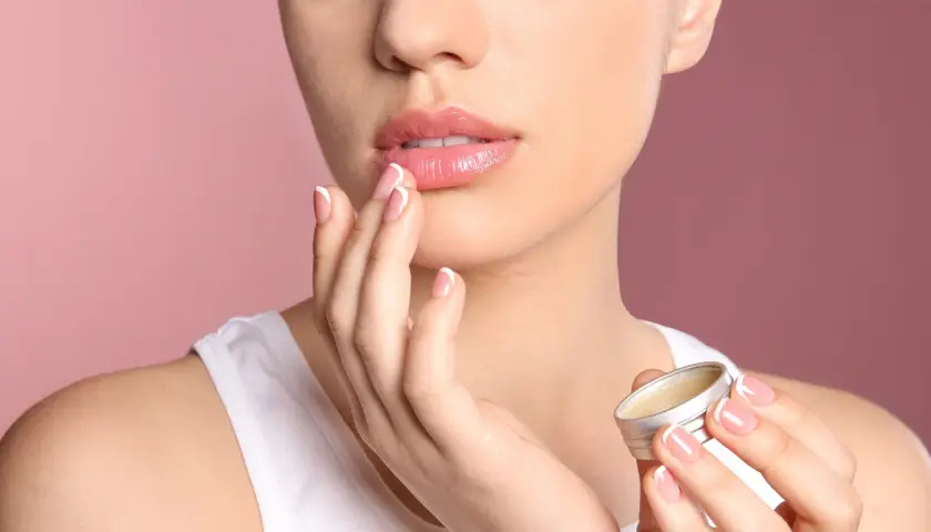 Mujer aplica bálsamo para aliviar labios secos. Sus manos y uñas perfectas contrastan con la suavidad de sus labios.