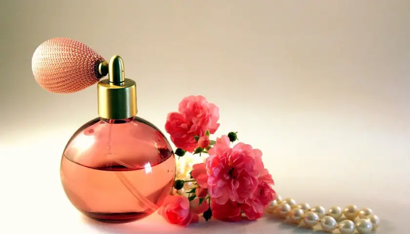 Frasco de perfume rosa con atomizador, rosas rosadas y collar de perlas. Un aroma que evoca la dulzura del almizcle que es.