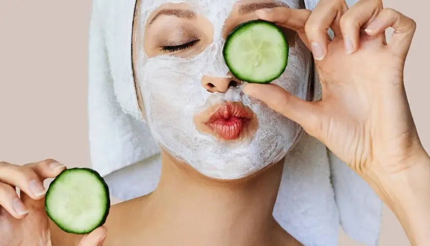 Mujer con mascarillas caseras para la cara y rodajas de pepino, lista para un spa en casa.