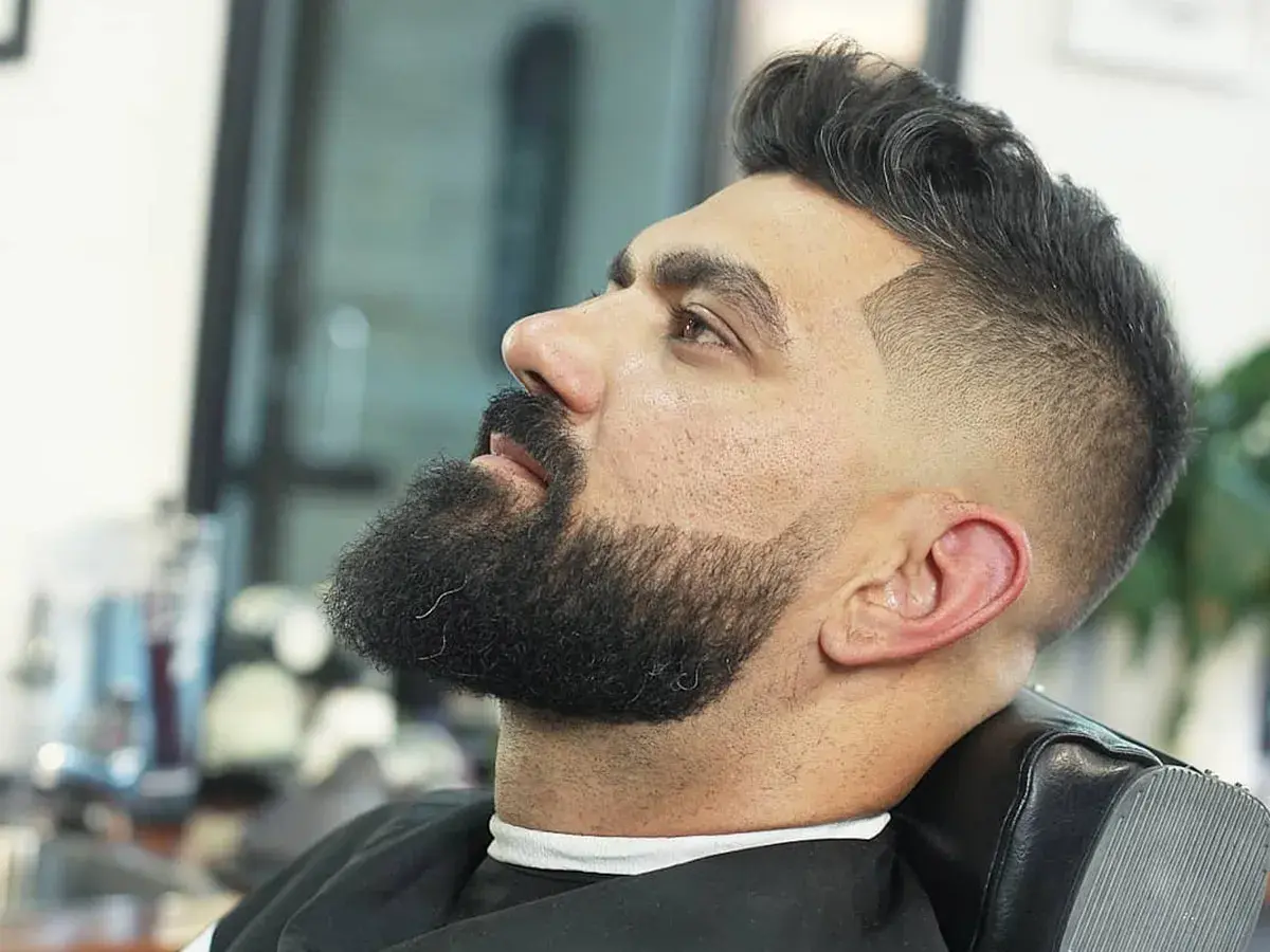 Hombre con barba y un moderno corte de pelo con degradado, uno de los tipos de corte de pelo hombre más populares.