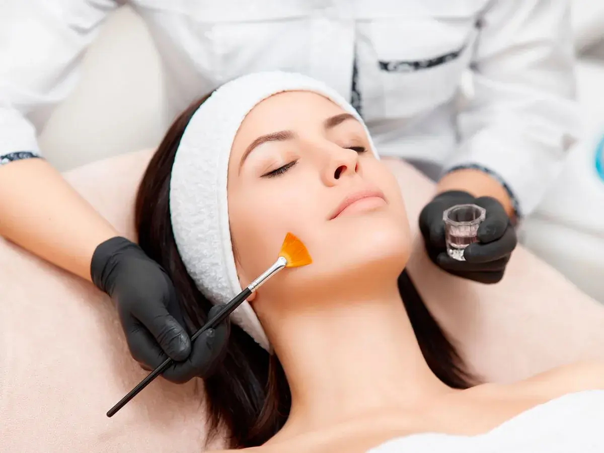 Una esteticista aplica un tratamiento de peeling facial con brocha a una mujer.