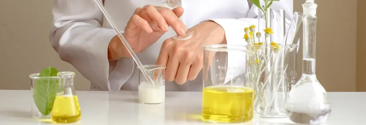 Manos de científico aplicando crema, con probetas y plantas. El cetearyl alcohol es clave en esta formulación.