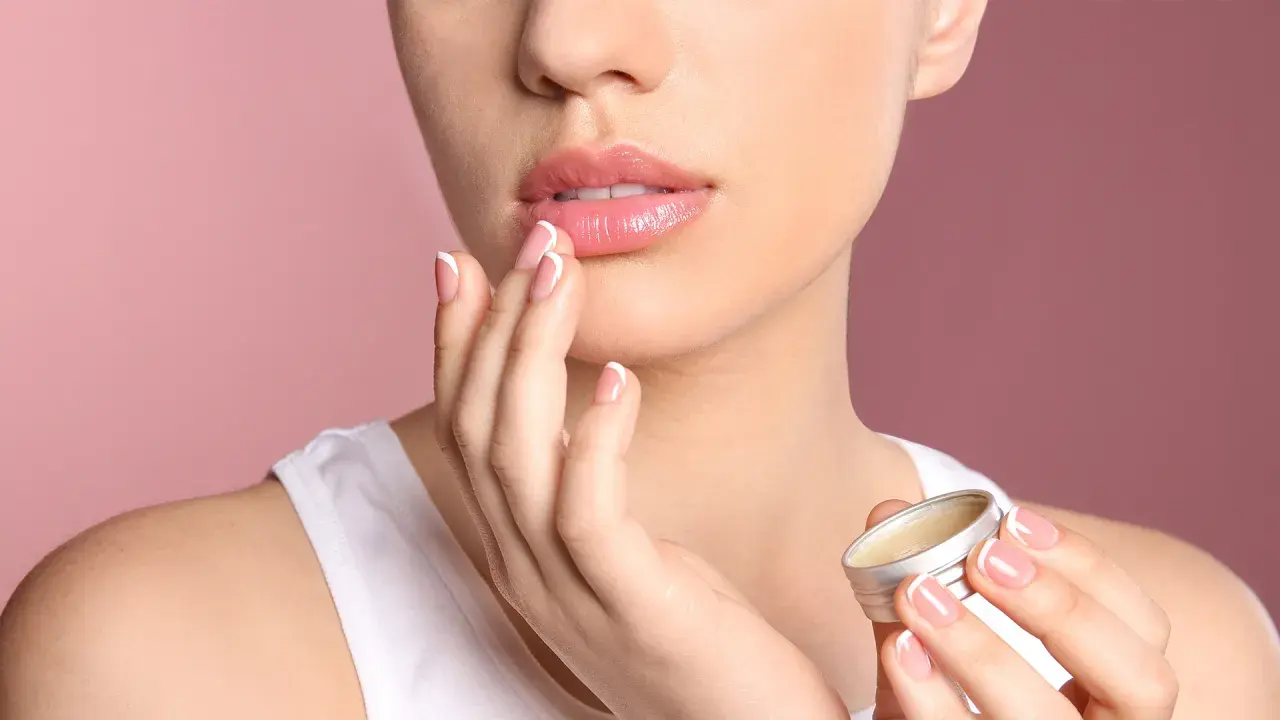 Mujer aplica bálsamo para aliviar labios secos. Sus manos y uñas perfectas contrastan con la suavidad de sus labios.