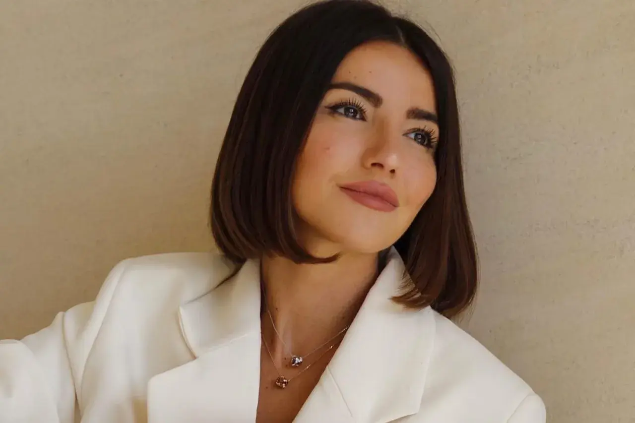Mujer con un corte de pelo **italian bob**, blazer blanco y collares delicados.