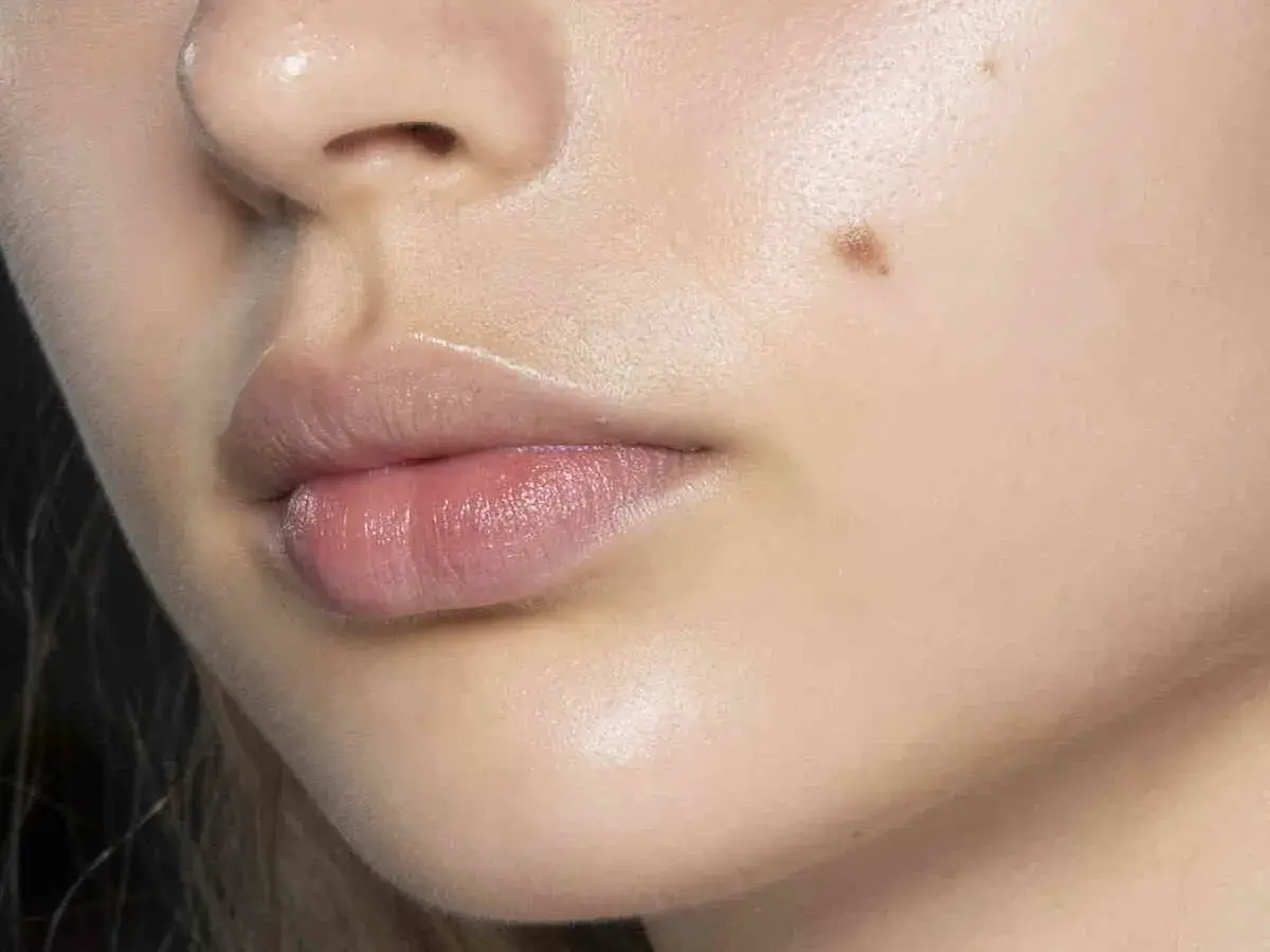 Labios rosados y piel luminosa con un lunar y un ligero vello facial.