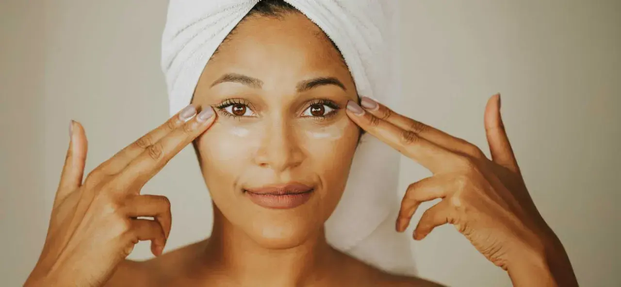 Mujer con toalla en la cabeza aplica crema con ceramida alrededor de sus ojos.