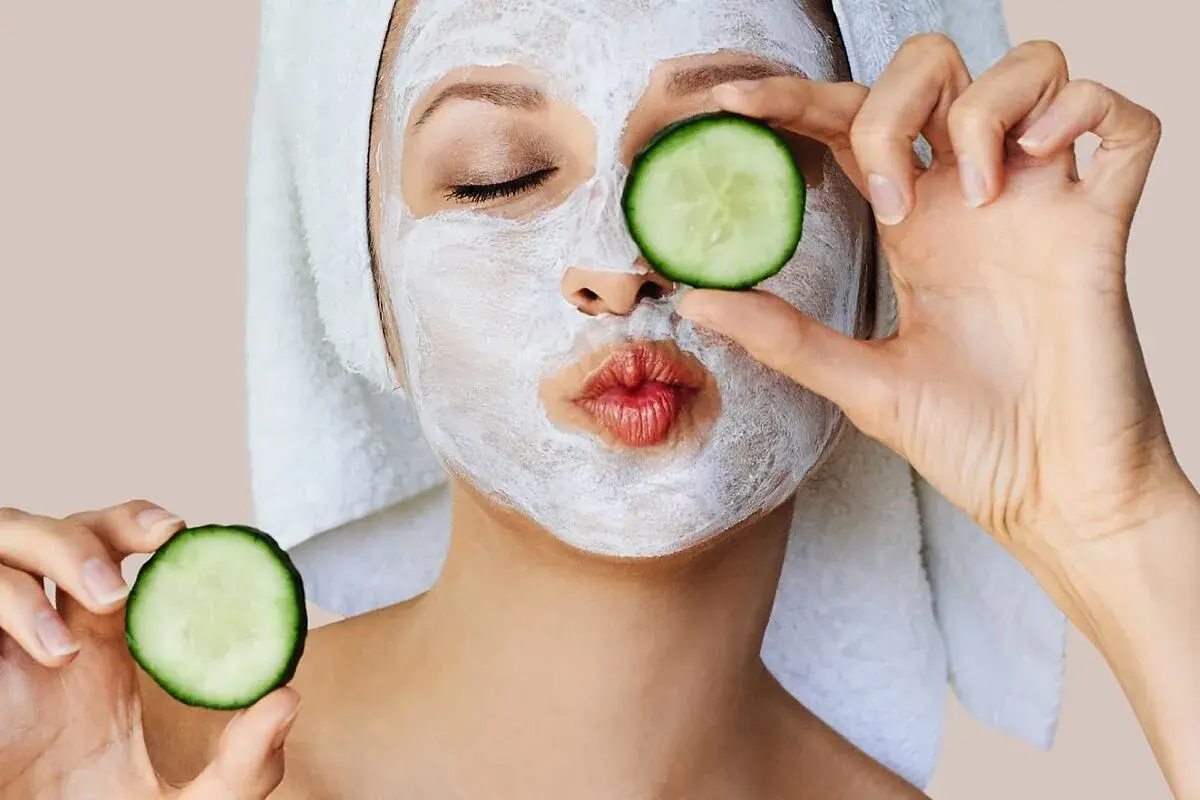 Mujer con mascarillas caseras para la cara y rodajas de pepino, lista para un spa en casa.